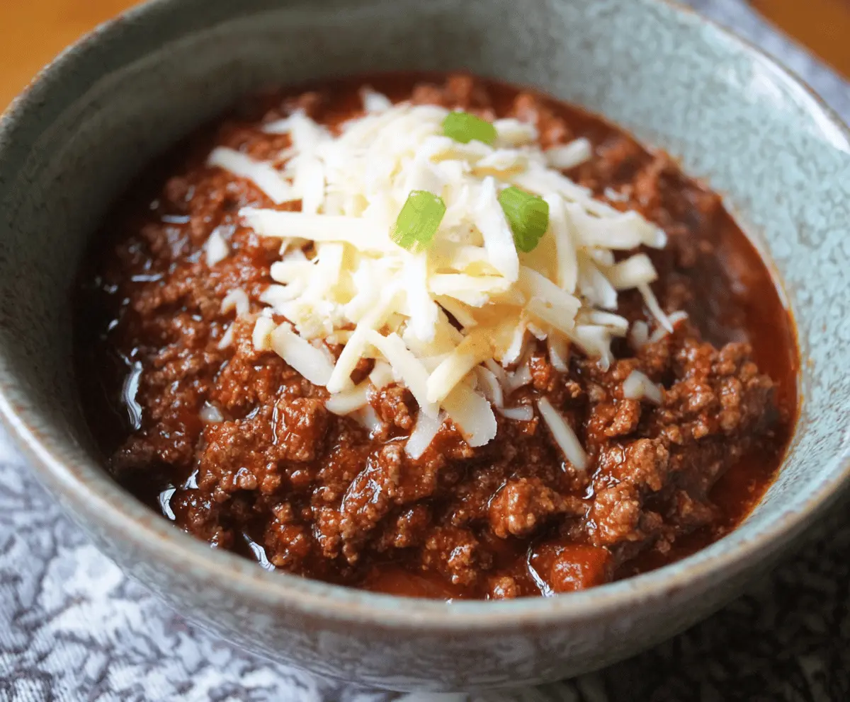 A steaming bowl of authentic Texas-style chili topped with shredded cheese and chopped onions, featuring rich, spicy ground beef chili served without beans.