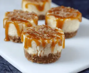 Mini salted caramel cheesecakes topped with caramel drizzle and sea salt on a decorative plate, perfect for dessert cravings