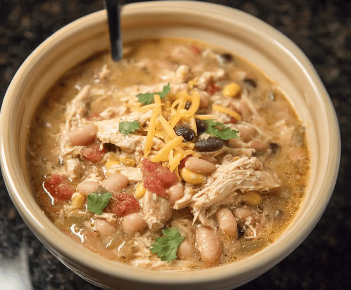 Creamy white chicken chili topped with shredded cheese and fresh cilantro in a bowl, featuring tender chicken, white beans, and spices for a flavorful comfort food meal.