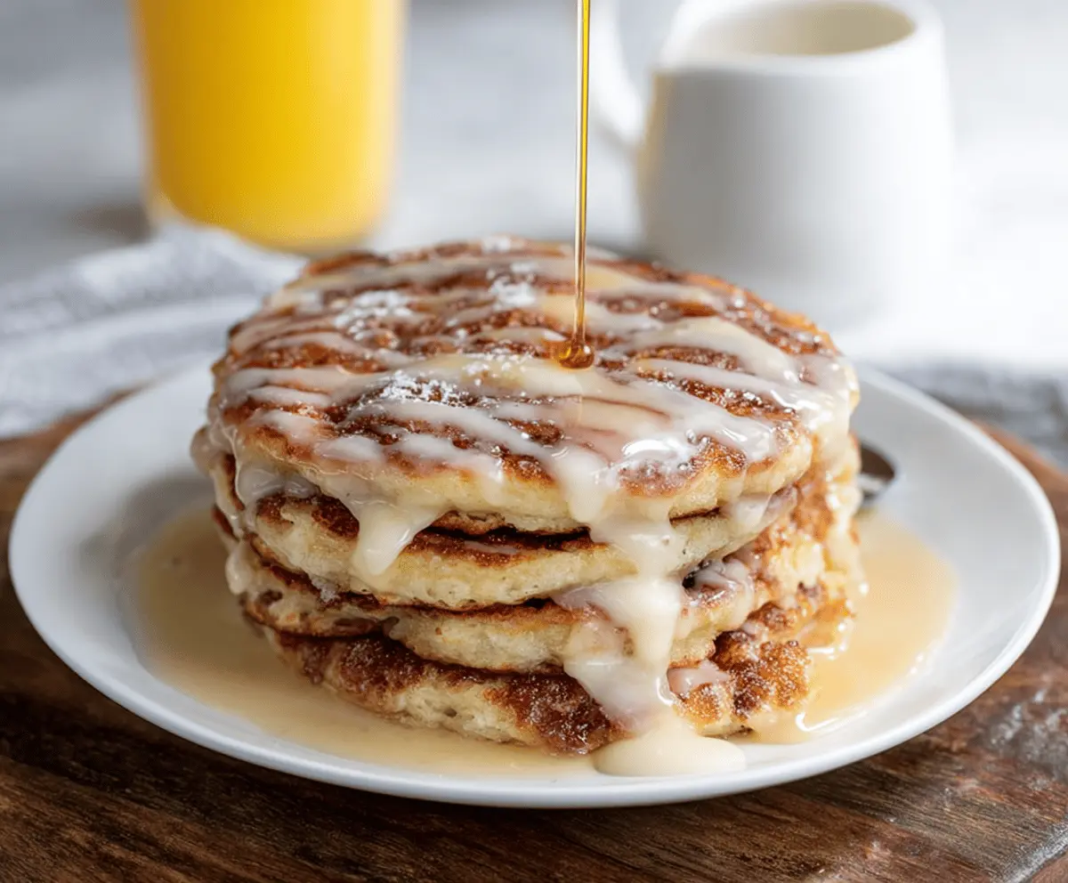 Delicious Maple Cinnamon Roll Pancakes drizzled with syrup, topped with cinnamon and chopped pecans.