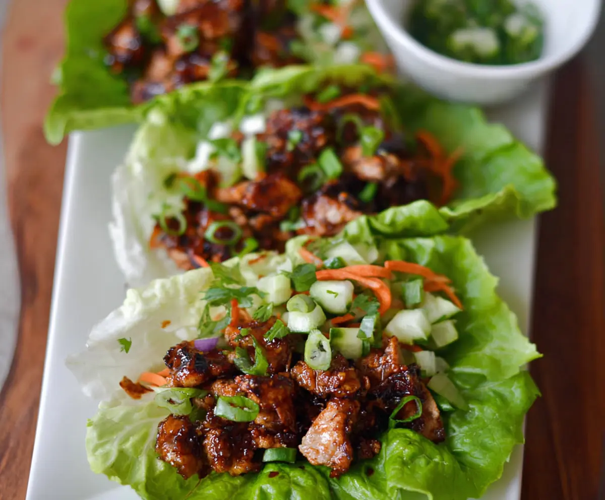 Hot Honey Chicken Lettuce Wraps on a plate with fresh greens and a drizzle of honey, showcasing a spicy and sweet chicken dish.