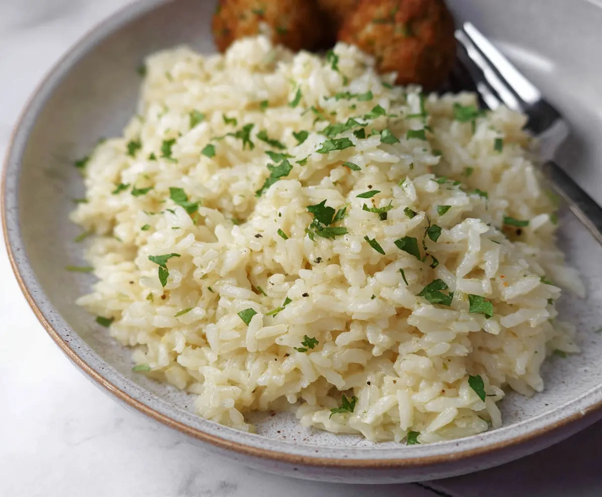 Delicious garlic parmesan rice served in a white bowl with fresh herbs on top.